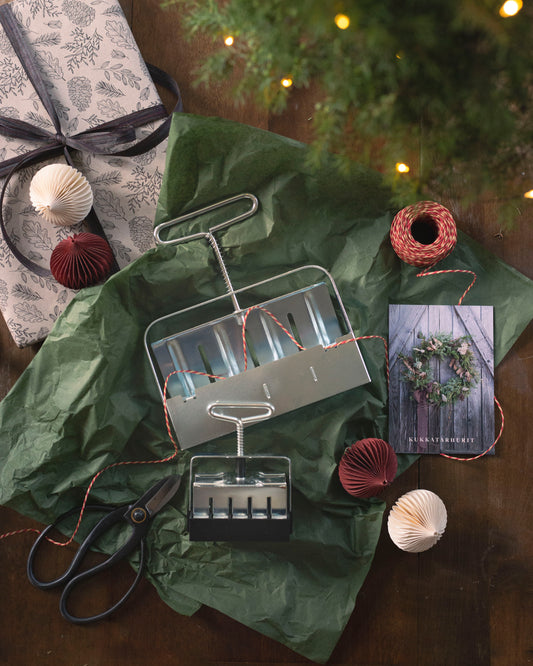 Soil Blocker Setti lahjapaketoinnin keskellä, ympärillä joulukoristeita, lahjanaru ja sakset. 